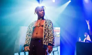 Juice WRLD on stage, a testament to his massive Juice WRLD Spotify streams. The artist, bathed in blue light, holds a microphone and a bottle.