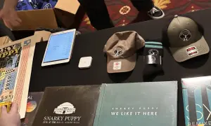 Snarky Puppy merchandise: vinyl records, hats, socks, and a tablet displaying a setlist.
