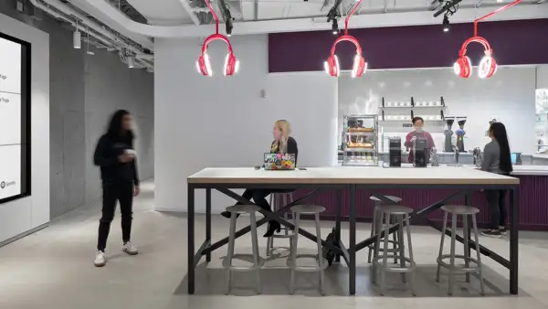 Inside Spotify Studios NYC, people gather around a communal table, with iconic headphone lights overhead.