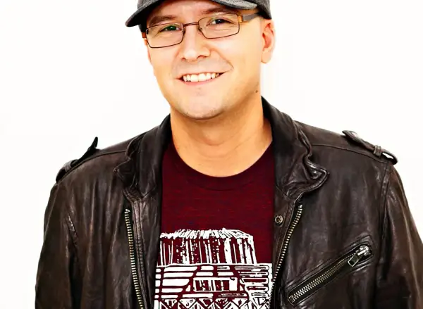 A smiling man in a leather jacket and cap, possibly inspired by the creative spirit behind Luke Laird songs.
