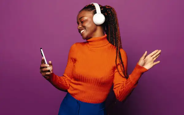 A woman with braids and headphones smiles, holding a phone. She's a visual representation of how to get your music on playlists.