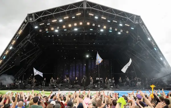 A massive crowd cheers at Glastonbury Festival, a testament to its huge capacity. Performers are on stage under a starry backdrop.